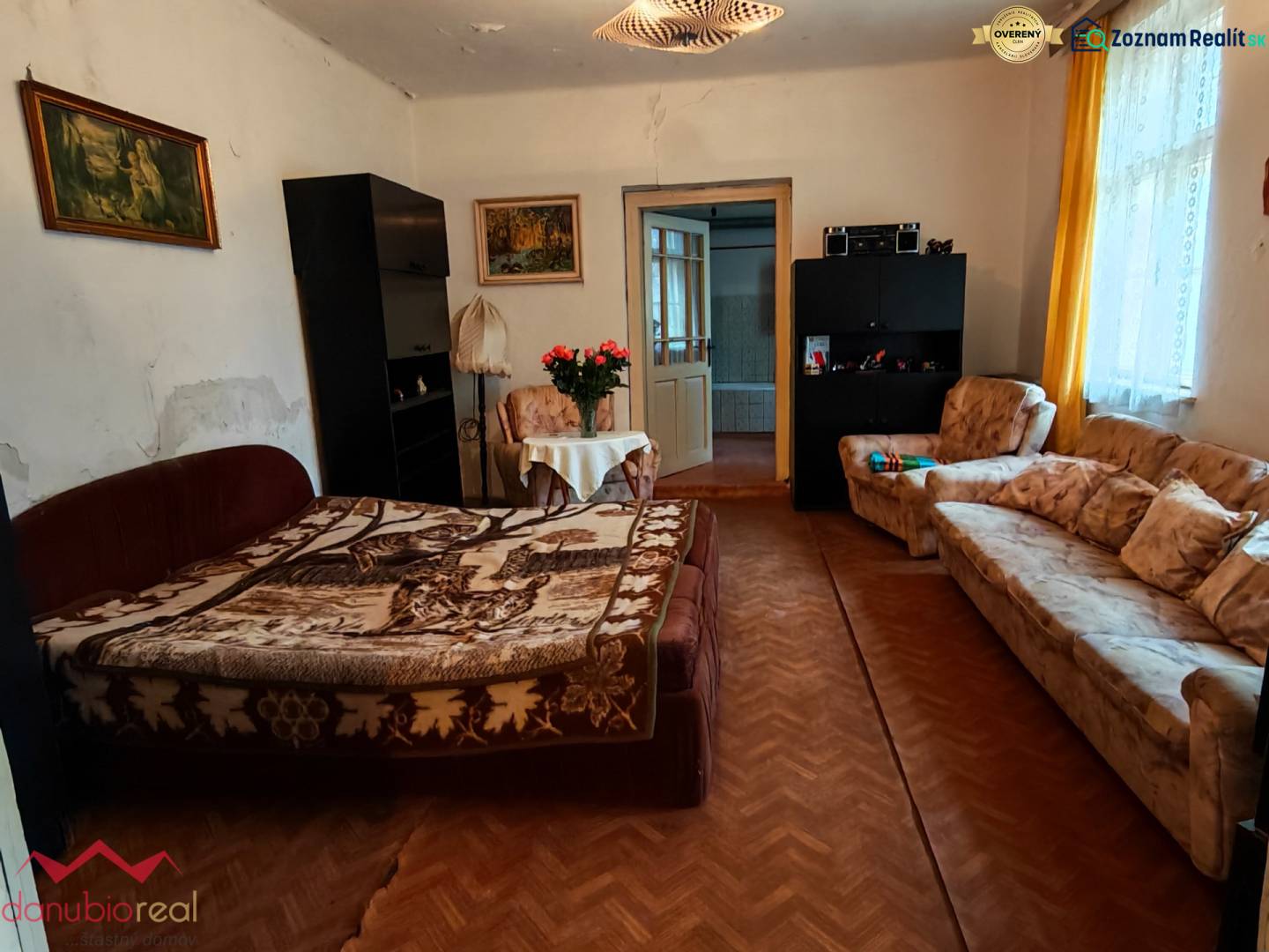 Obývací pokoj v rodinném domě s květinami, pohovkou a podlahou s dřevěným dekorem.