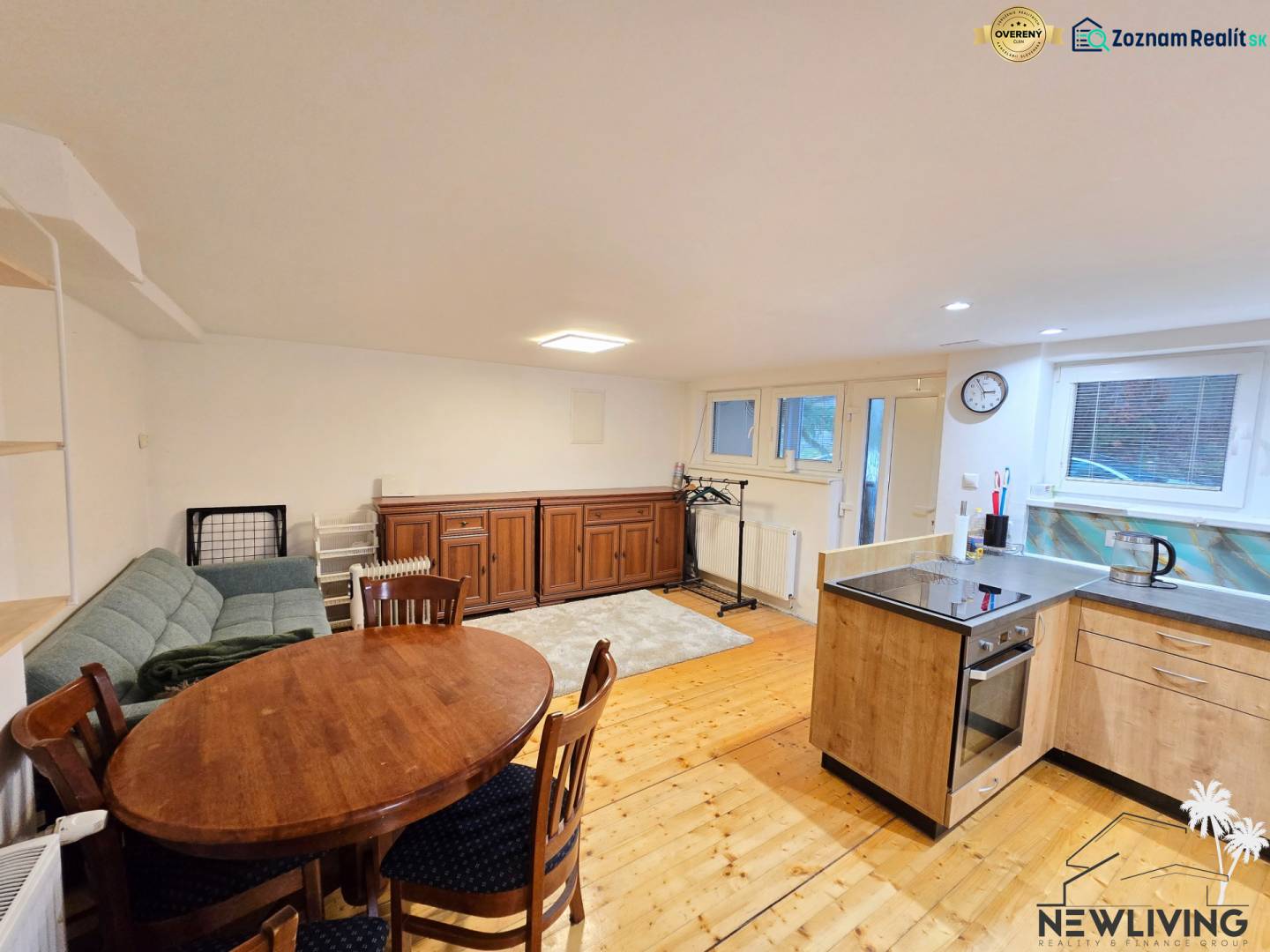 Obývací pokoj v jednopokojovém bytě s podlahou s dřevěným dekorem, sedačkou a jídelním stolem.