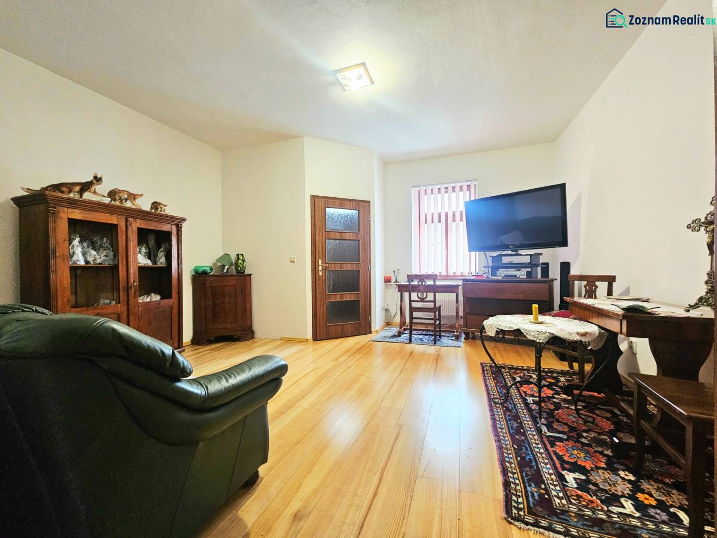 Obývací pokoj v 3-pokojovém bytě s podlahou s dřevěným dekorem, vybavený sedačkou a televizorem.