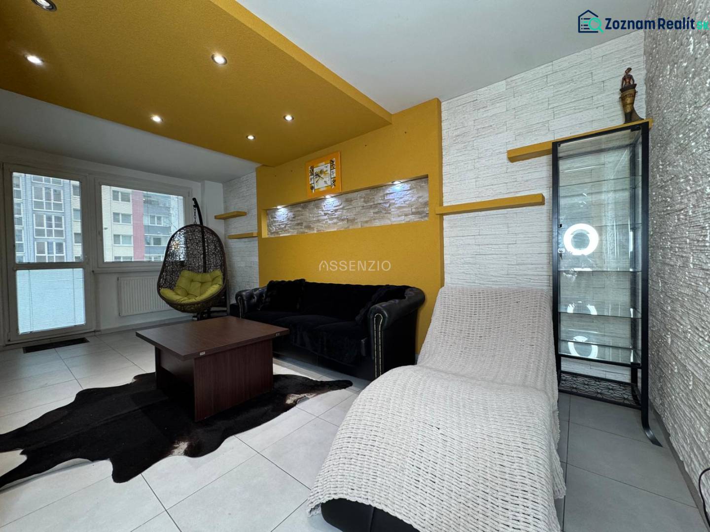 Obývací pokoj v 3-pokojovém bytě s barevnými stěnami, prosklenou vitrínou a závěsným křeslem.