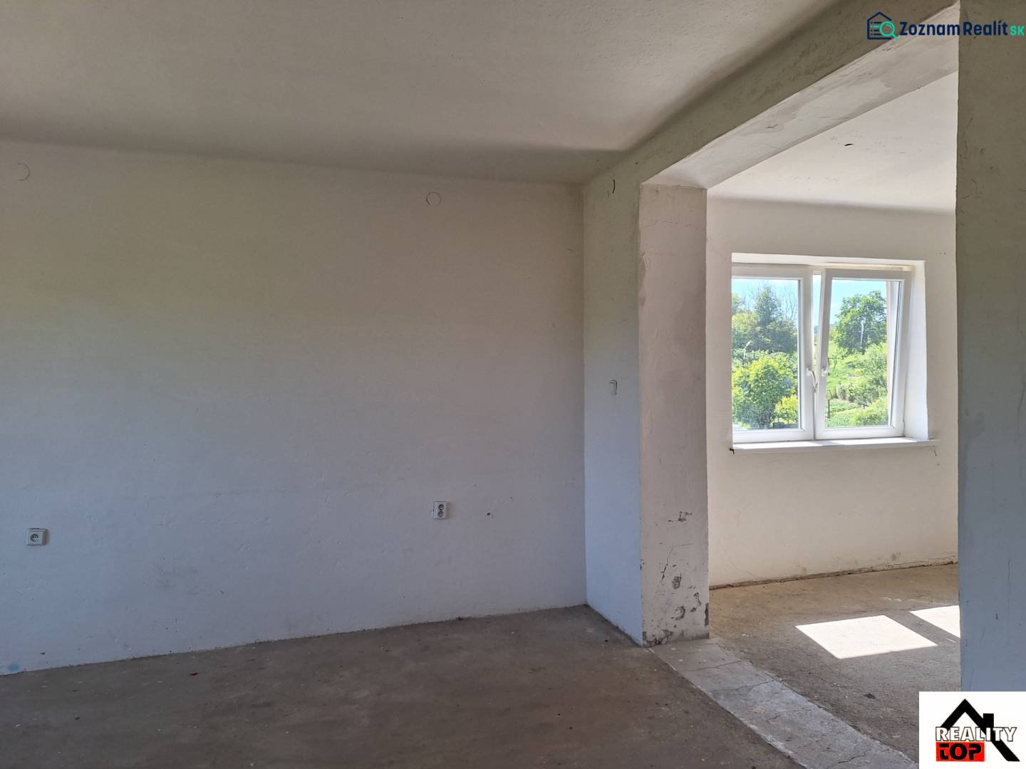 Nezařízená místnost v rodinném domě s výhledem do zahrady přes plastové okno.