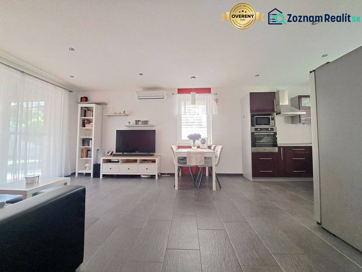 Obývací pokoj s TV, kuchyní a jídelním stolem, podlaha s dřevěným dekorem.