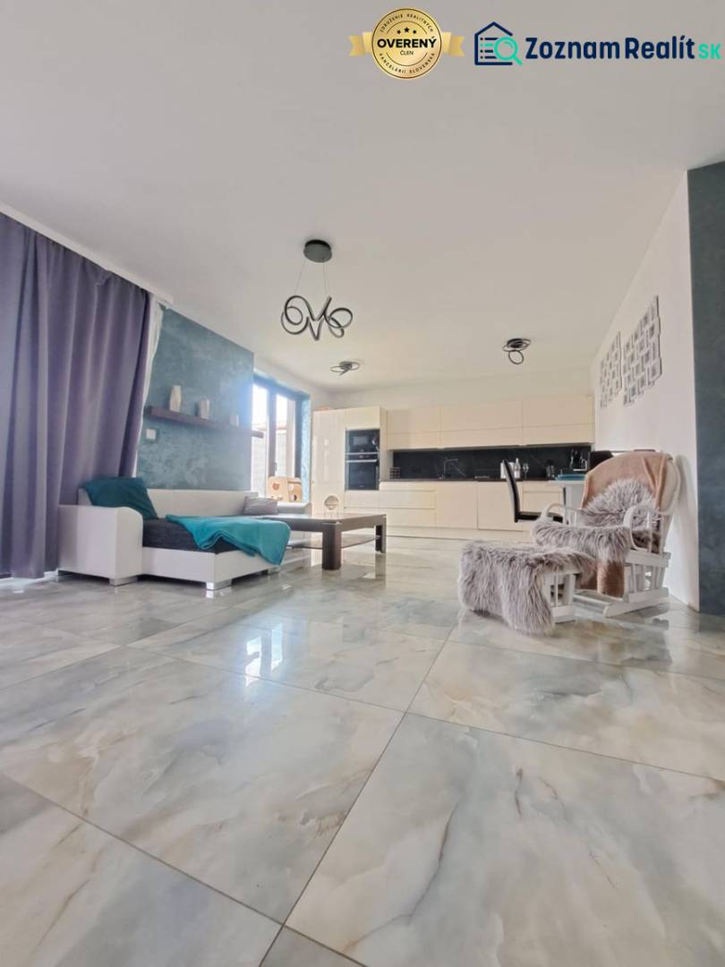 Obývací pokoj s velkými okny a světlými dlaždicemi v rodinném domě.