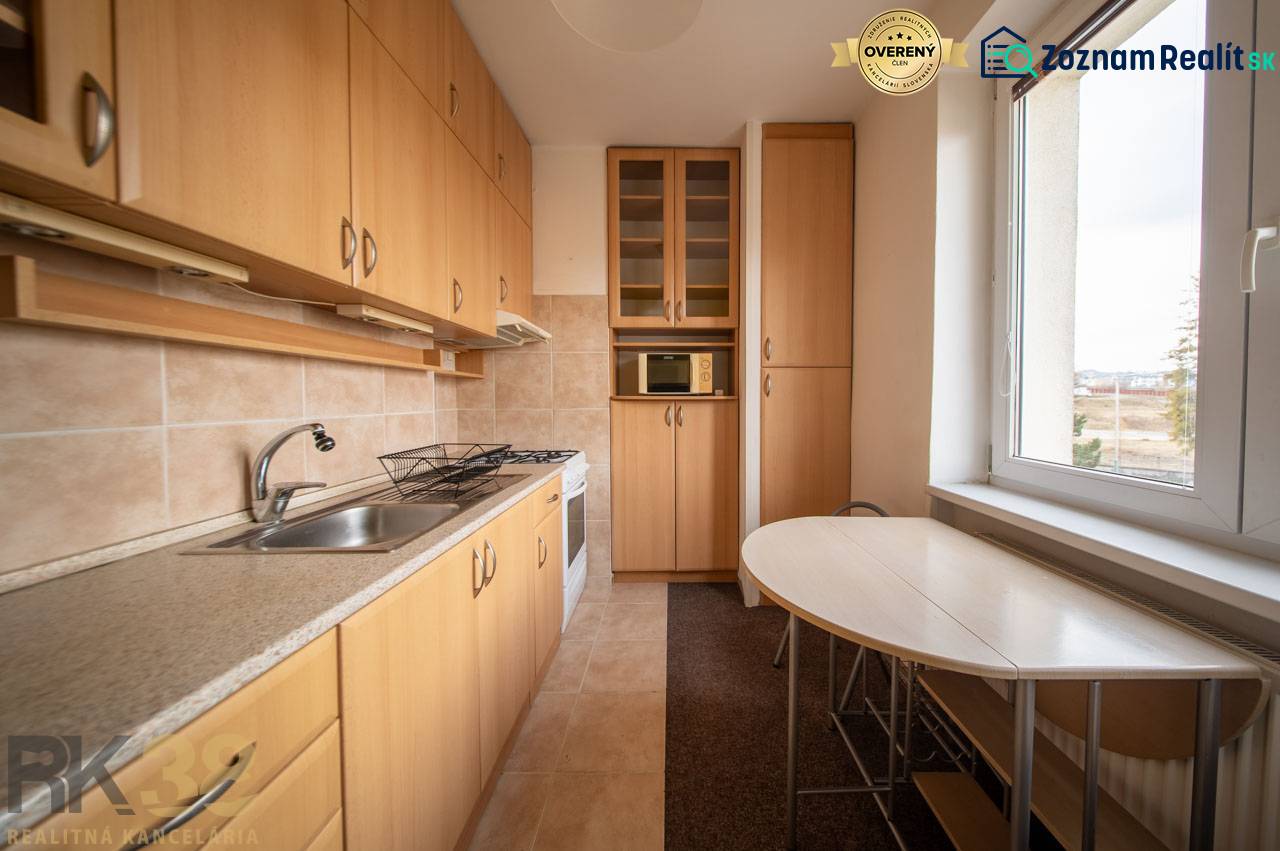 Kuchyně v 2-pokojovém bytě s podlahou s dřevěným dekorem, světlým nábytkem a stolem u okna.