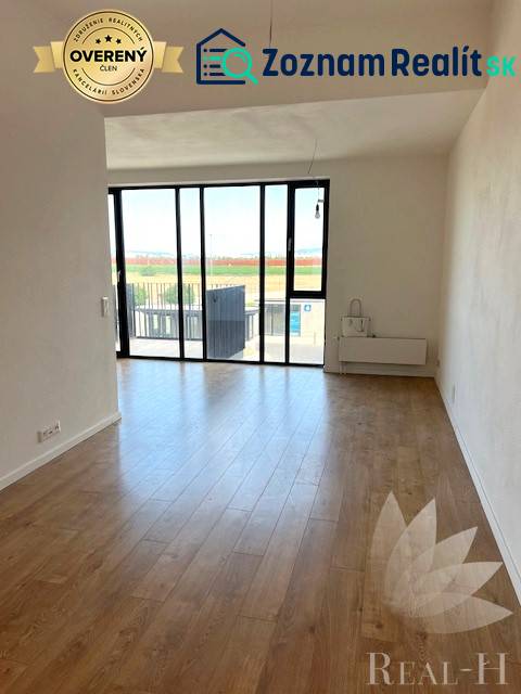 Světlý obývací pokoj s velkými okny a podlahou s dřevěným dekorem v 2-pokojovém bytě.