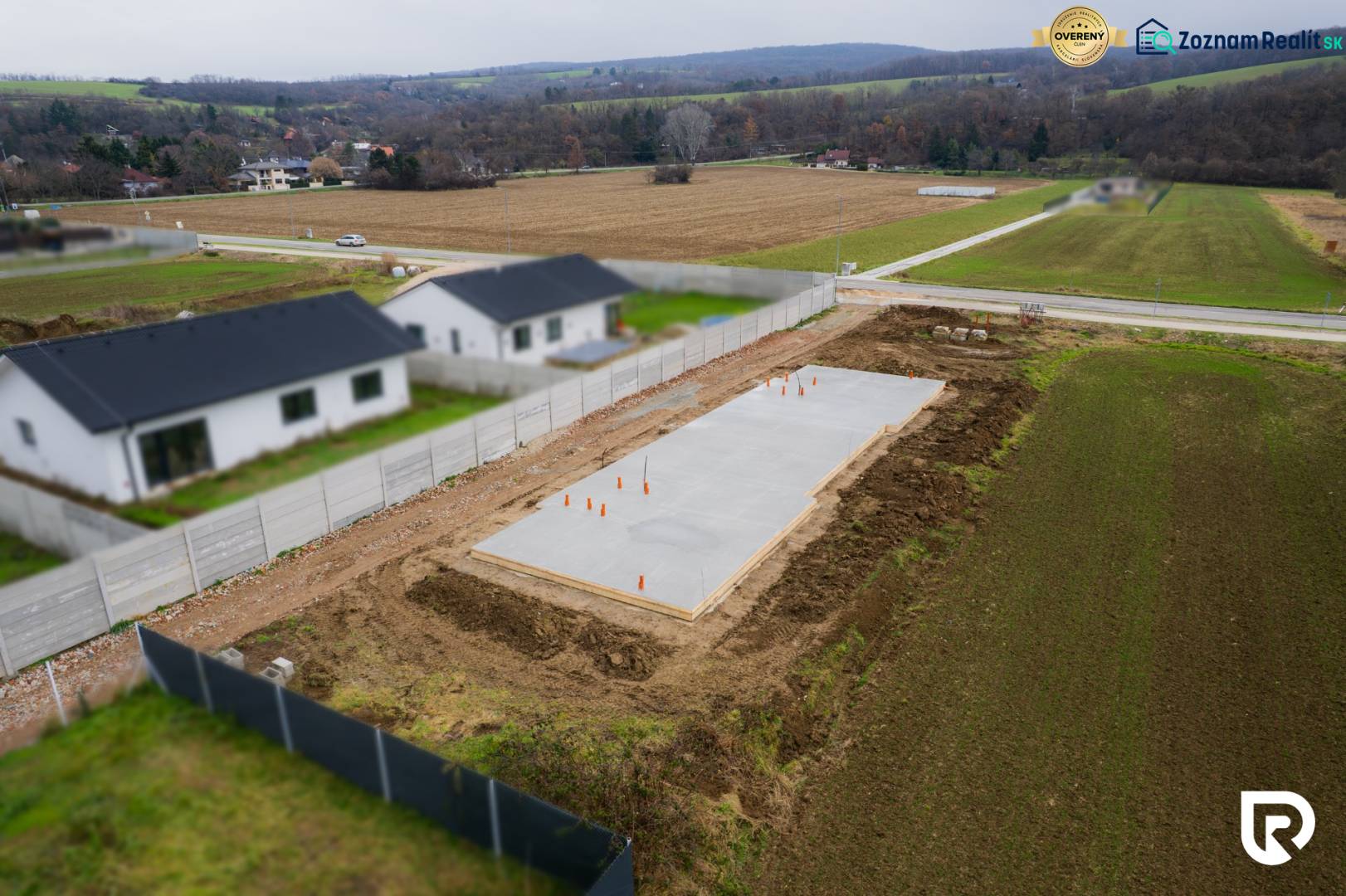 Základy rodinného domu v Sokolovcích, obklopené poli a sousedními domy.