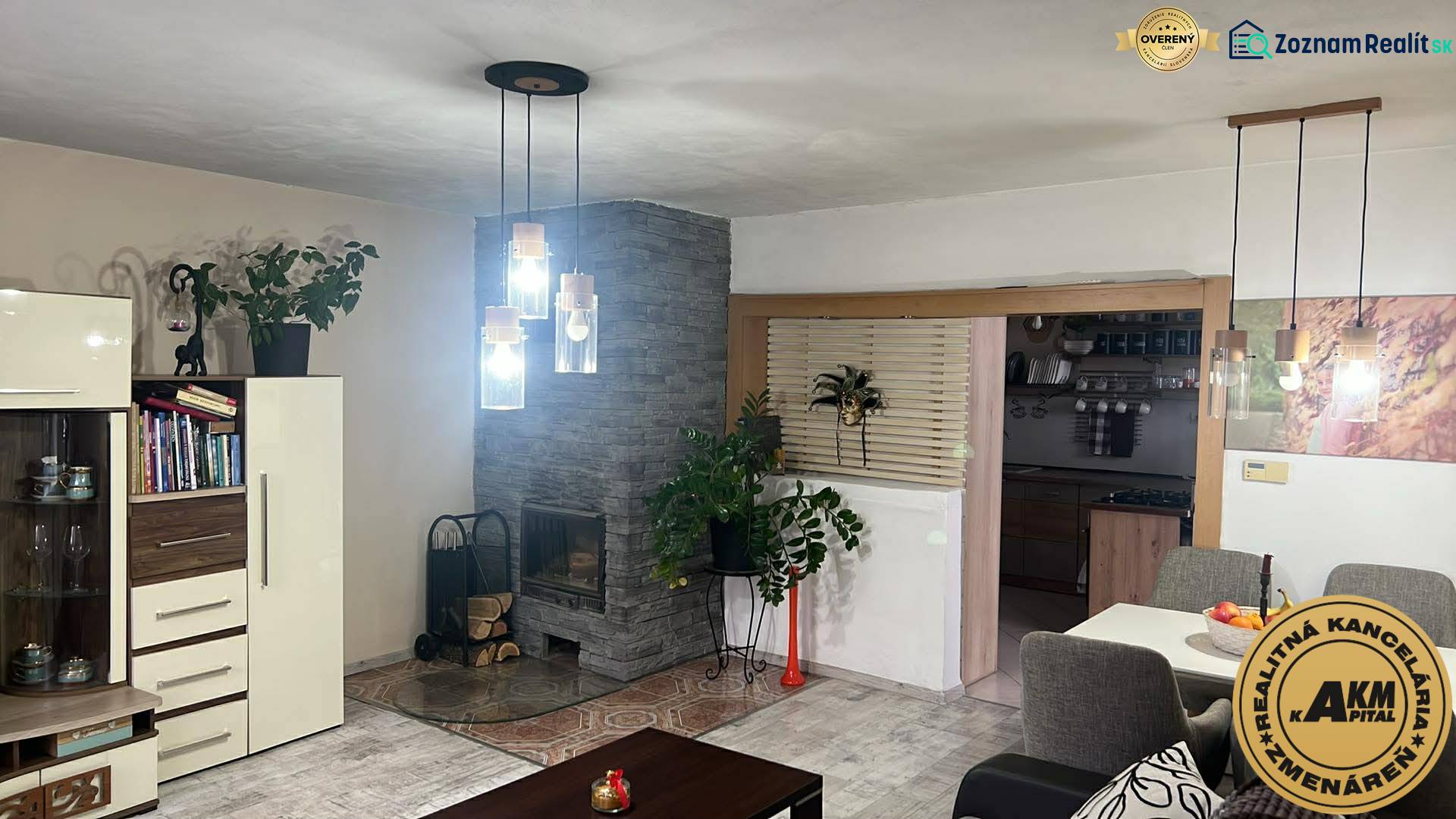 Interiér rodinného domu s krbem, závěsnými svítidly a podlahou s dřevěným dekorem.