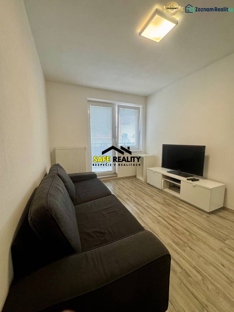 Obývací pokoj v 2pokojovém bytě s pohovkou, televizí a podlahou s dřevěným dekorem.