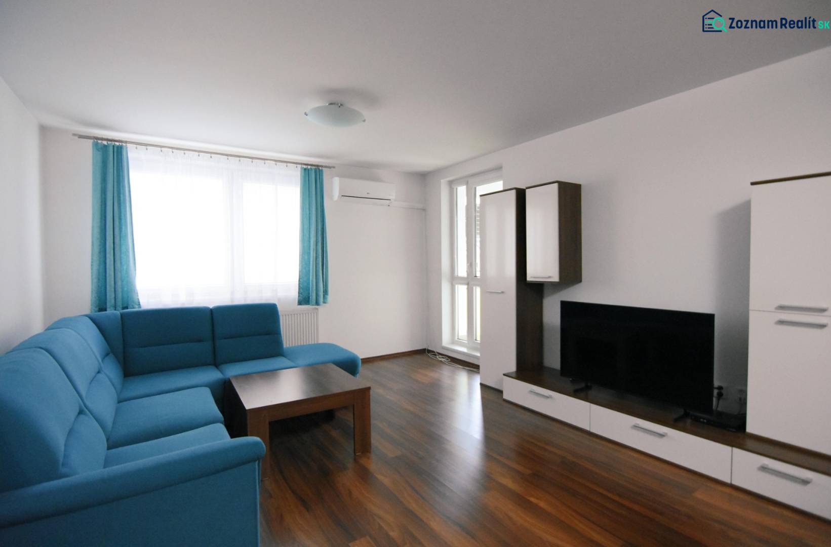 Obývací pokoj v 2-pokojovém bytě s modrou pohovkou a podlahou s dřevěným dekorem.
