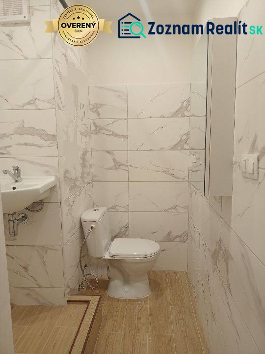 Koupelna garsonky s toaletou, umyvadlem a podlahou s dřevěným dekorem.