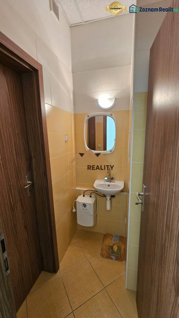 Koupelna v obchodních prostorách s umyvadlem a zrcadlem, obložená světlými kachličkami.