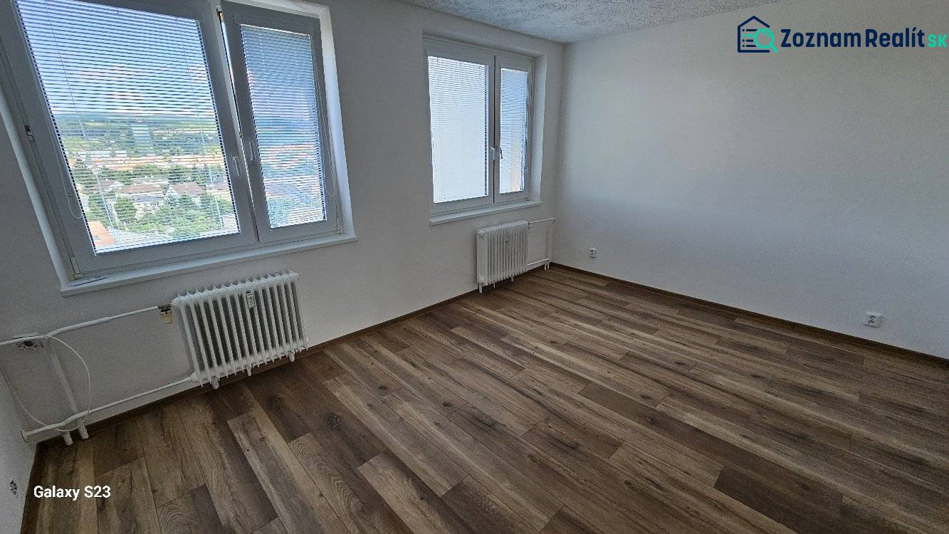 Prostorný pokoj v 3-pokojovém bytě s podlahou s dřevěným dekorem a velkými okny.