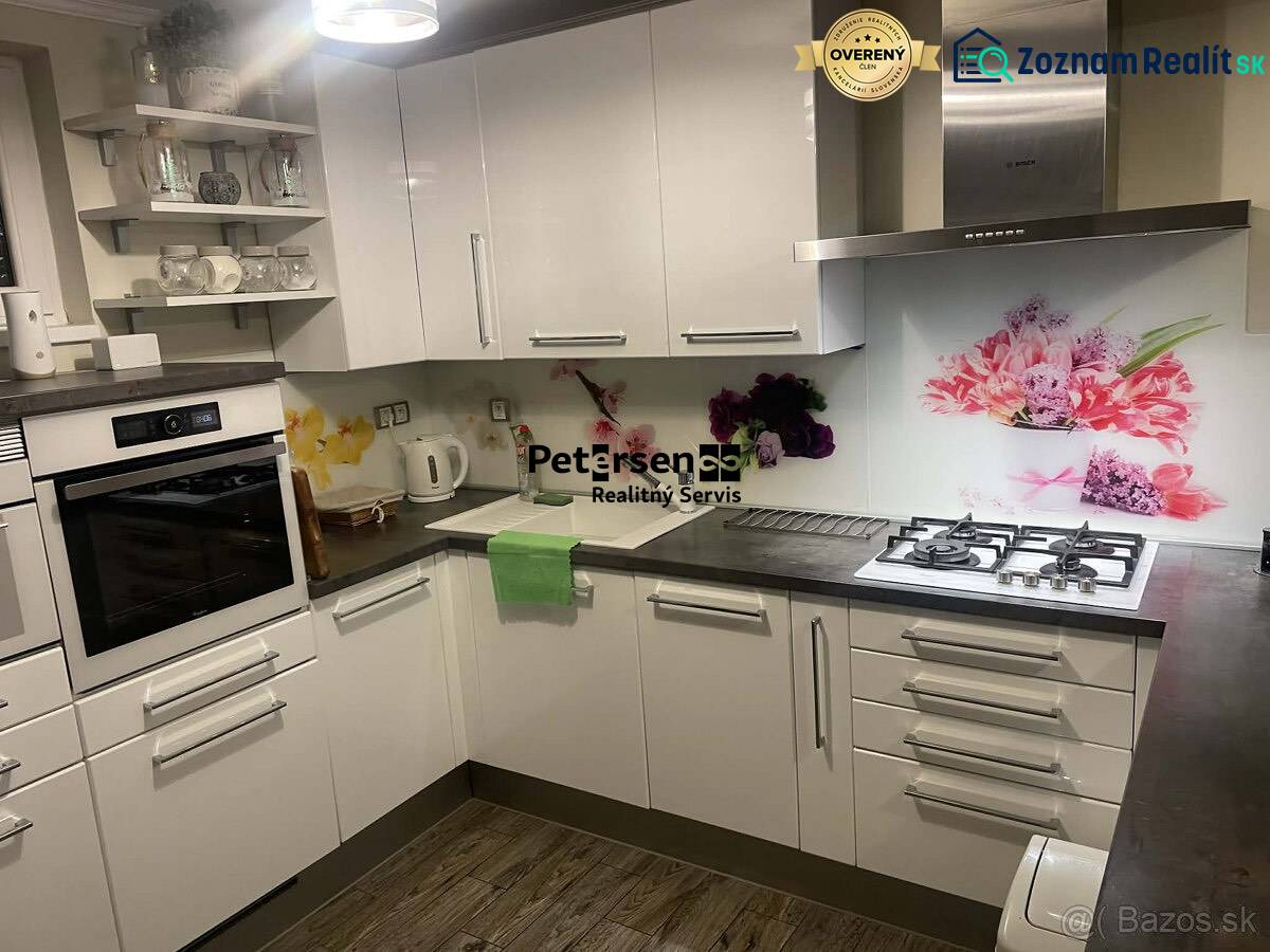 Kuchyně v rodinném domě s bílými skříňkami, dekorativním obkladem a podlahou s dřevěným dekorem.