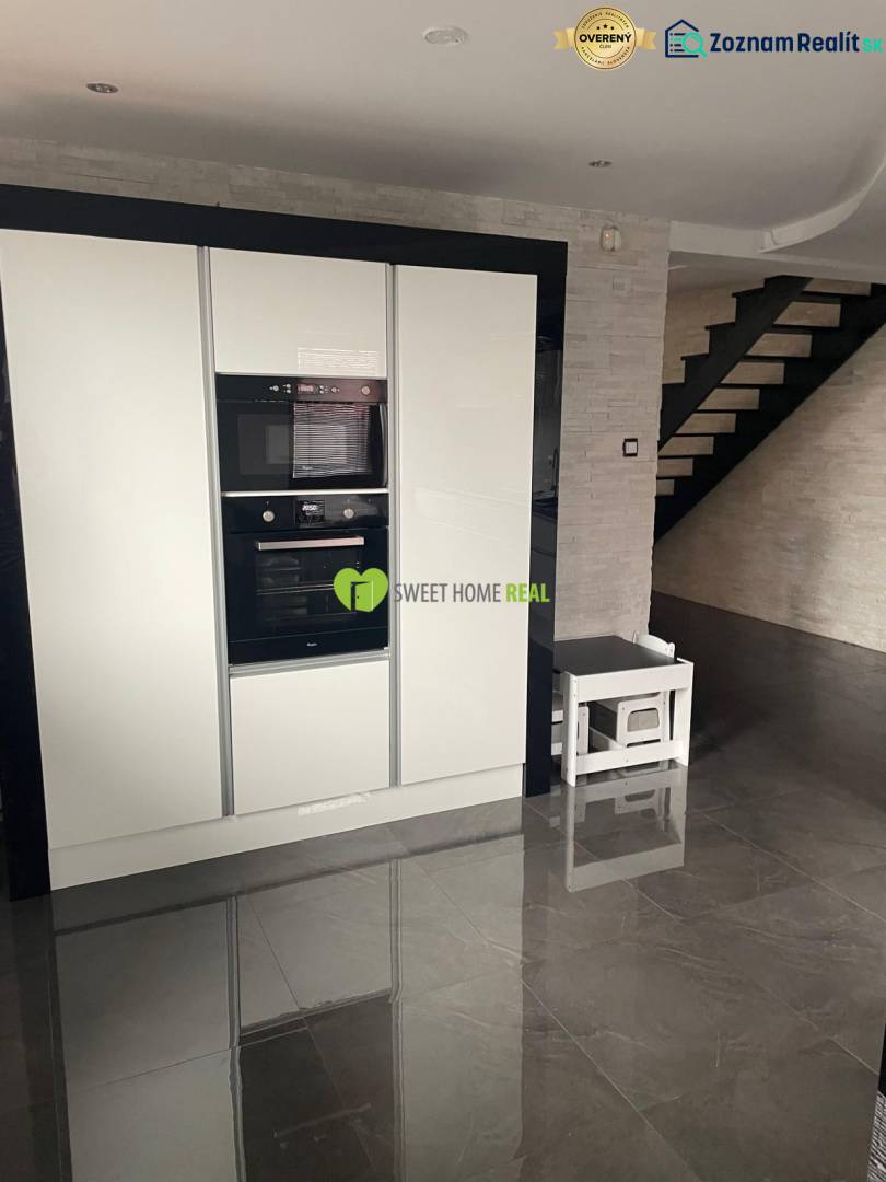 Kuchyně v rodinném domě s lesklou černou podlahou a bílými spotřebiči.