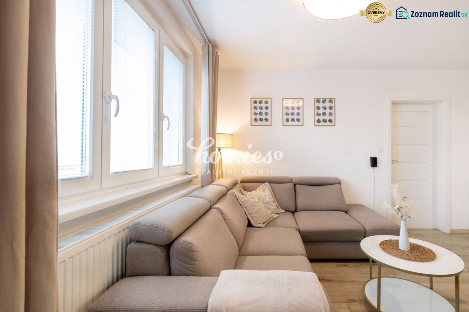 Obývací pokoj v 2-pokojovém bytě s pohodlnou sedačkou a dekoracemi na stěně.