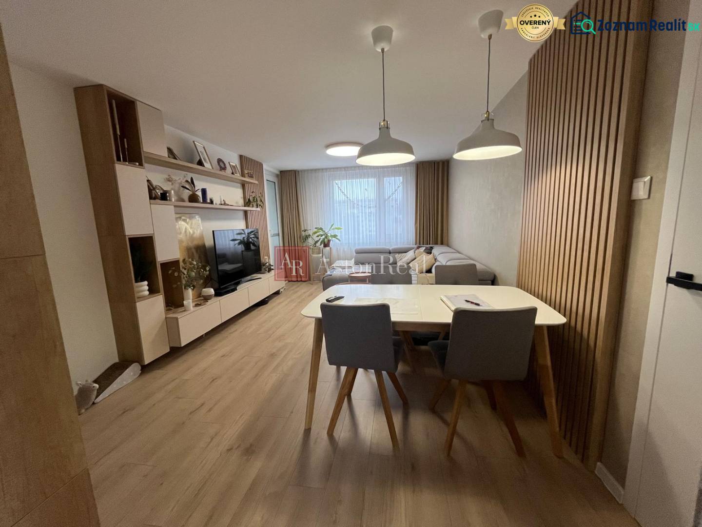 Obývací pokoj ve 4-pokojovém bytě s pohovkou, TV, jídelním stolem a podlahou s dřevěným dekorem.