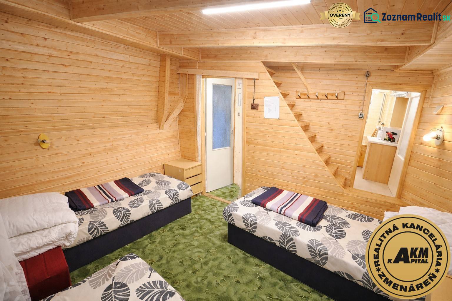 Součástí interiéru chaty jsou dvě postele, dřevěné obklady a zelený koberec.