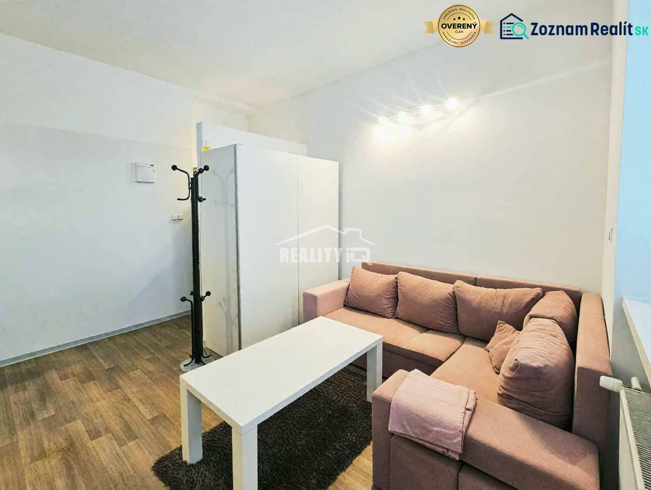 Garsonka s rohovou sedačkou, bílým stolkem a podlahou s dřevěným dekorem.