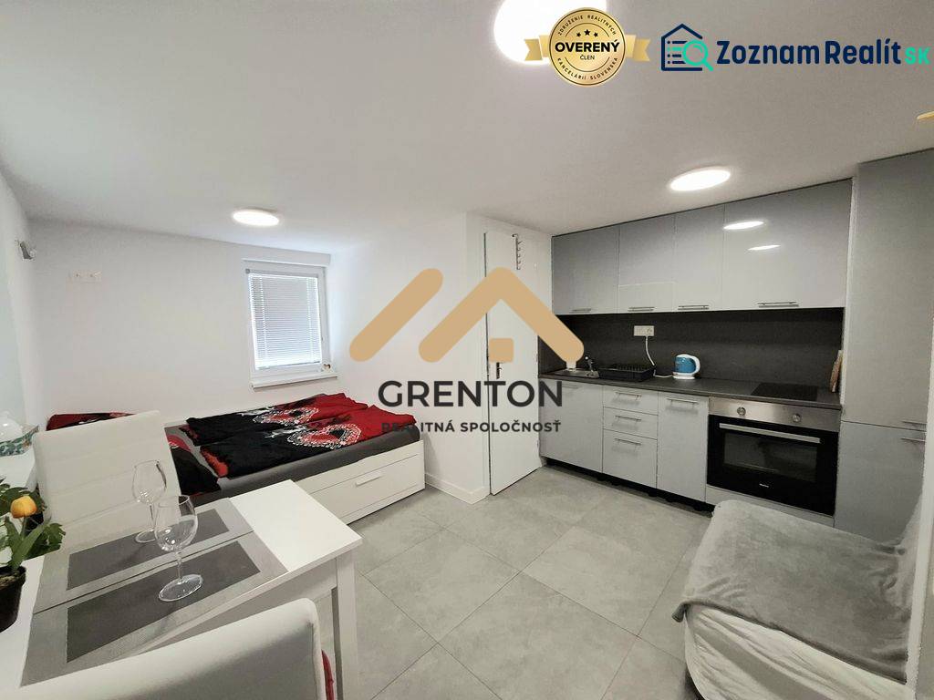 Kuchyňský kout a lůžko v chatě s obkladem šedé barvy a vybavením.