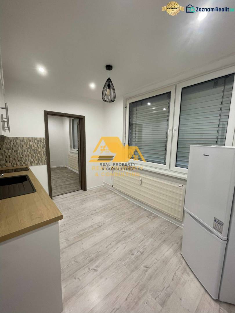 Kuchyně v 1-pokojovém bytě s podlahou s dřevěným dekorem a bílými elektrospotřebiči.