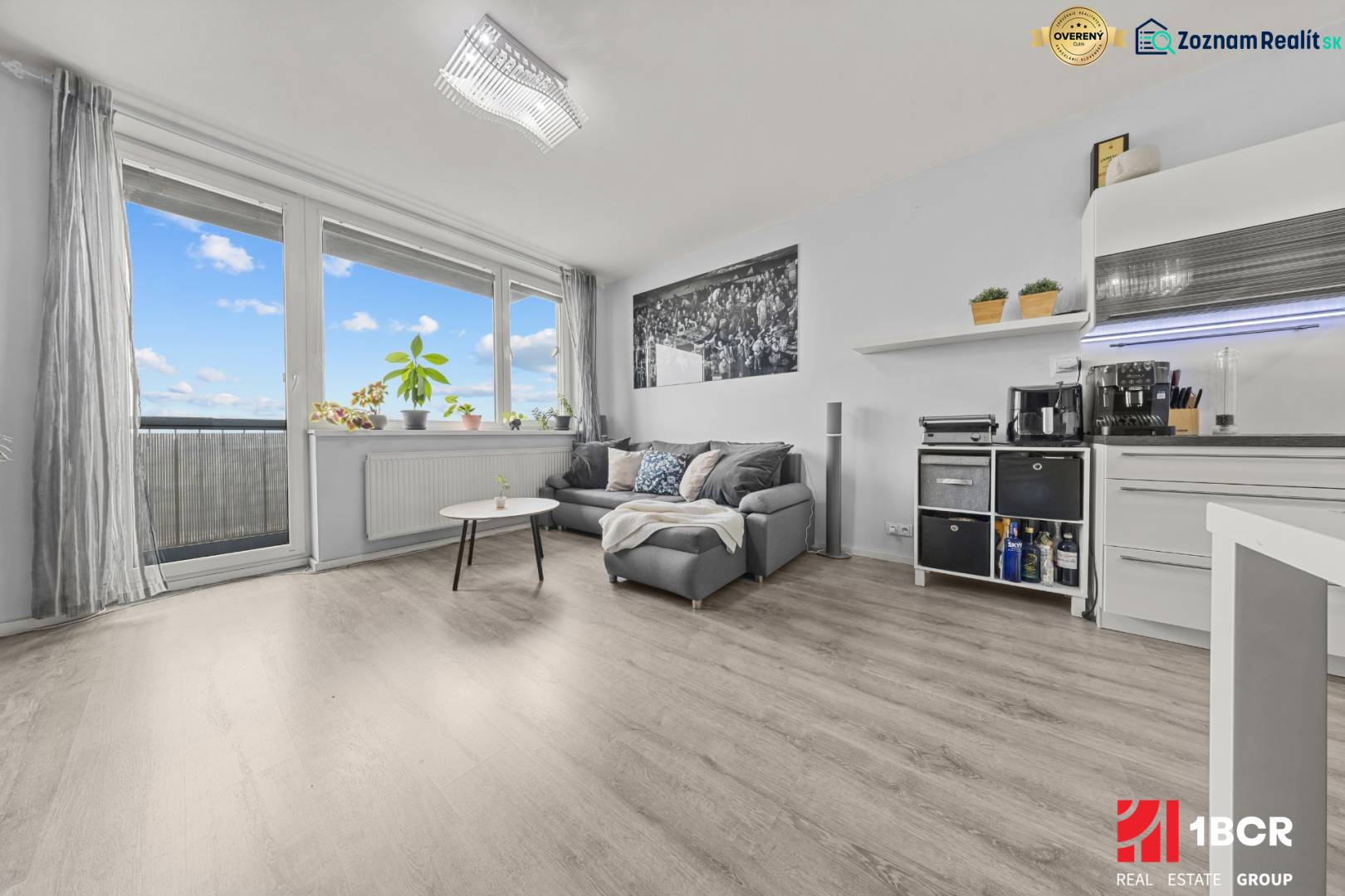 Obývací část 2-pokojového bytu s pohovkou, stolkem a podlahou s dřevěným dekorem.