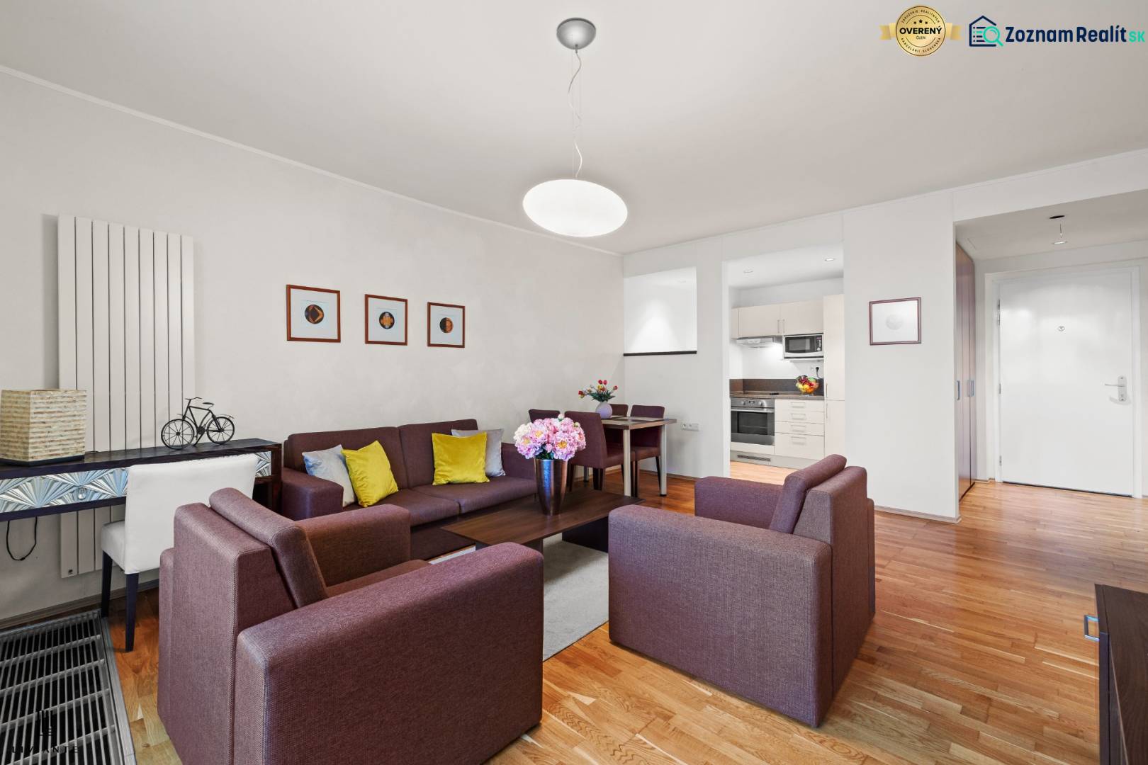 Obývací pokoj v 2-pokojovém bytě s podlahou s dřevěným dekorem, pohodlnými sedačkami a kuchyňským koutem.