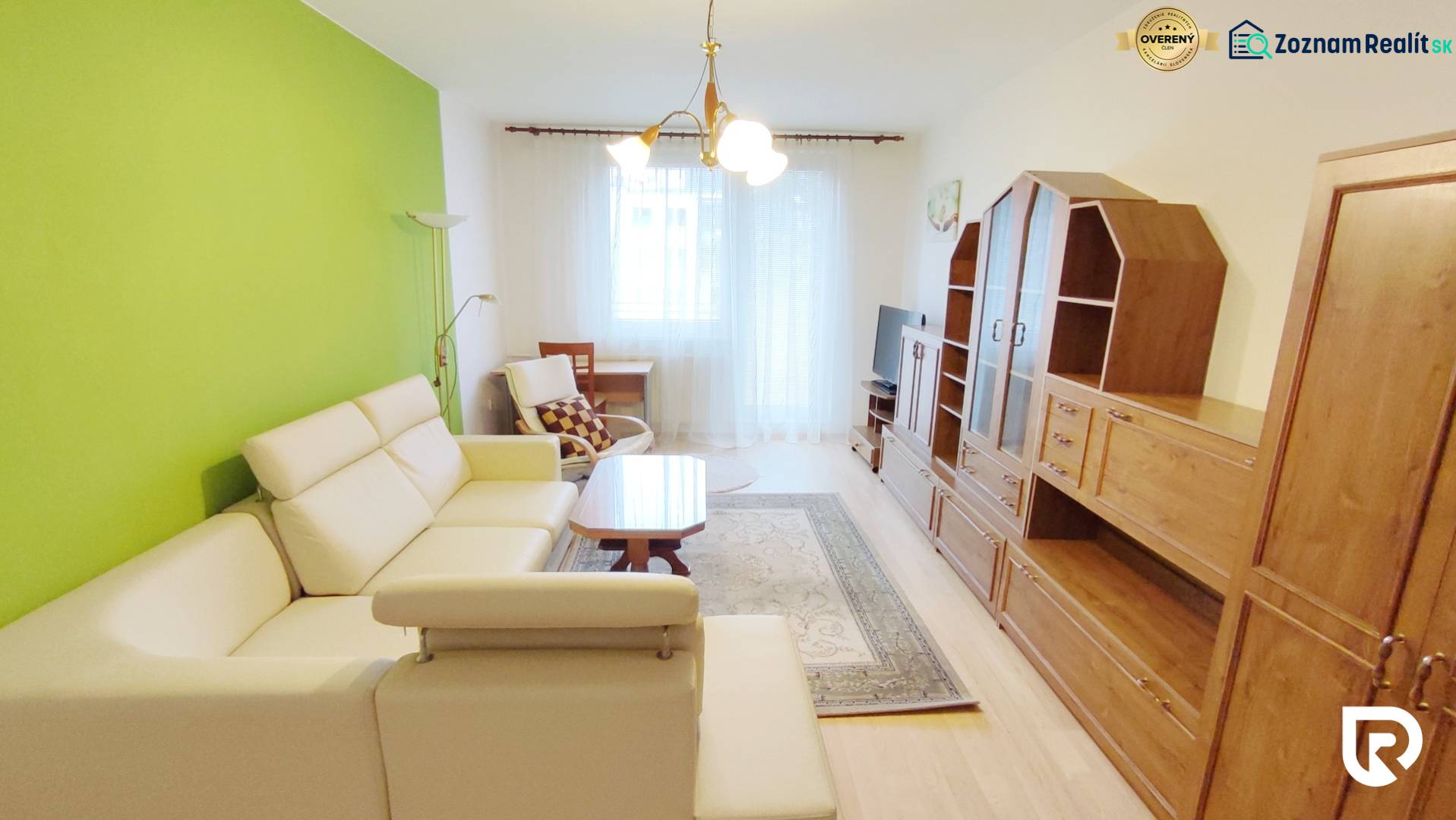 Obývací pokoj v 2-pokojovém bytě s krémovou sedačkou, zelenou stěnou a sestavou.