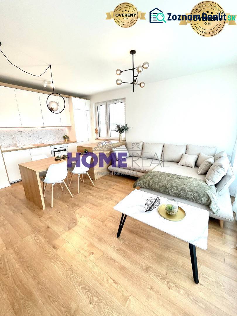 Obývací pokoj s kuchyní v 3-pokojovém bytě, světlá sedačka, podlaha s dřevěným dekorem.