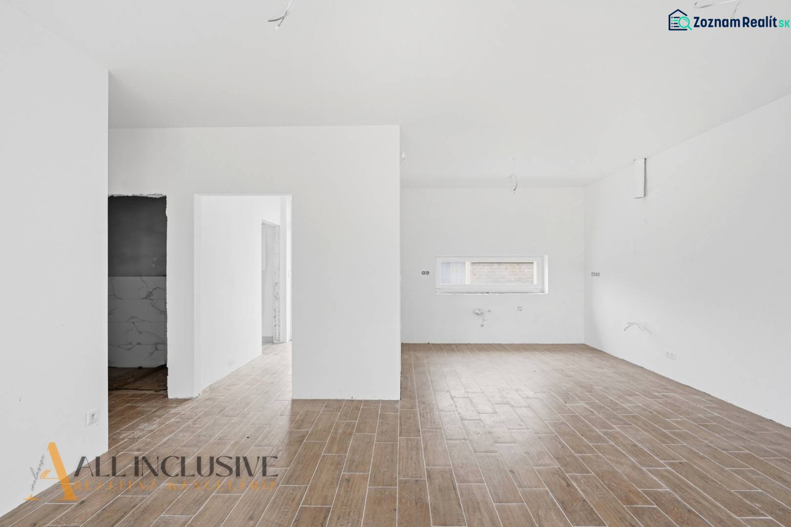 Interiér rodinného domu s podlahou s dřevěným dekorem a bílými stěnami.