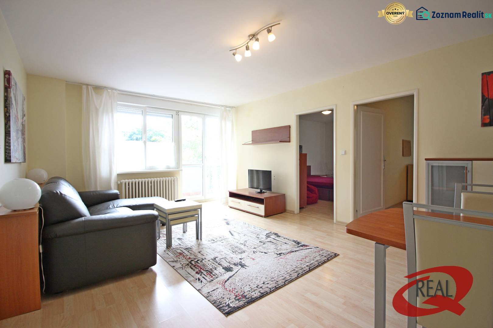 Obývací pokoj 3pokojového bytu s pohovkou, stolkem a televizí na podlaze s dřevěným dekorem.