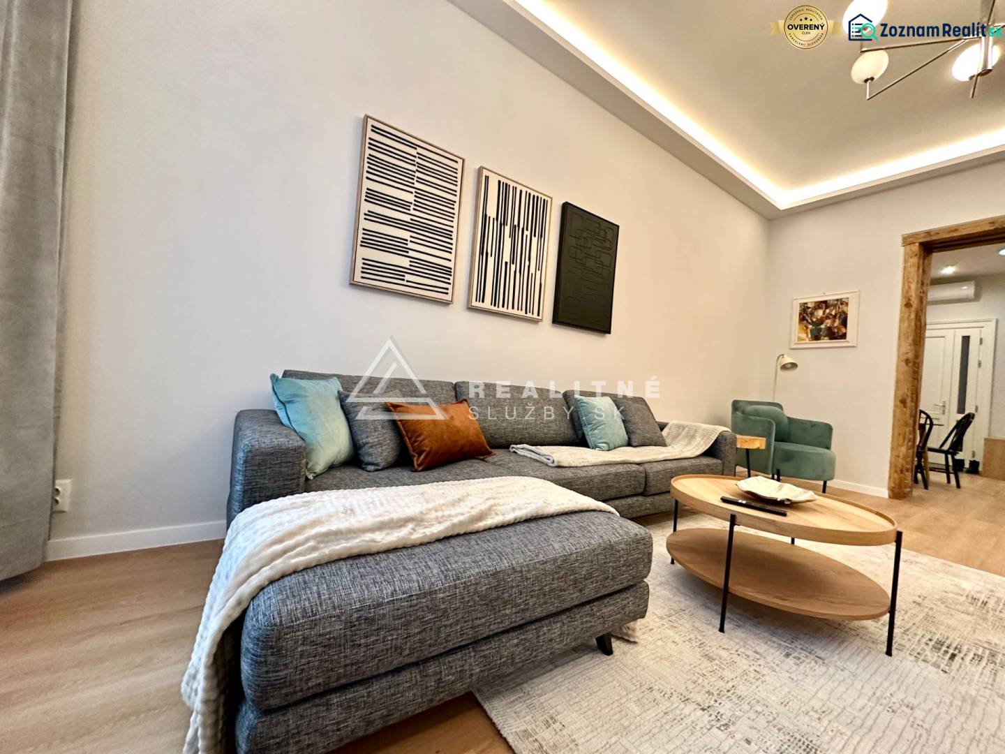 Obývací pokoj s pohovkou, podlahou s dřevěným dekorem a uměleckými díly ve 2pokojovém bytě.