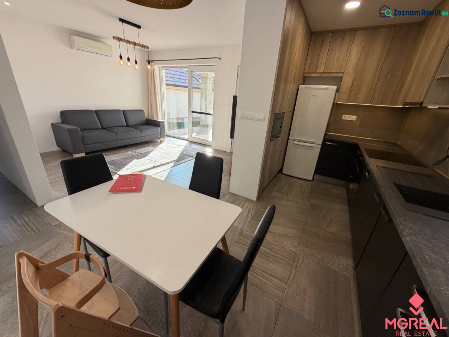 Interiér rodinného domu s kuchyní, jídelním stolem, sedačkou a podlahou s dřevěným dekorem.