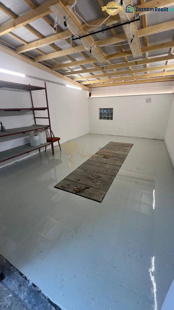 Garáže s regály a světlými stěnami, podlaha s jámou na opravu vozidel.