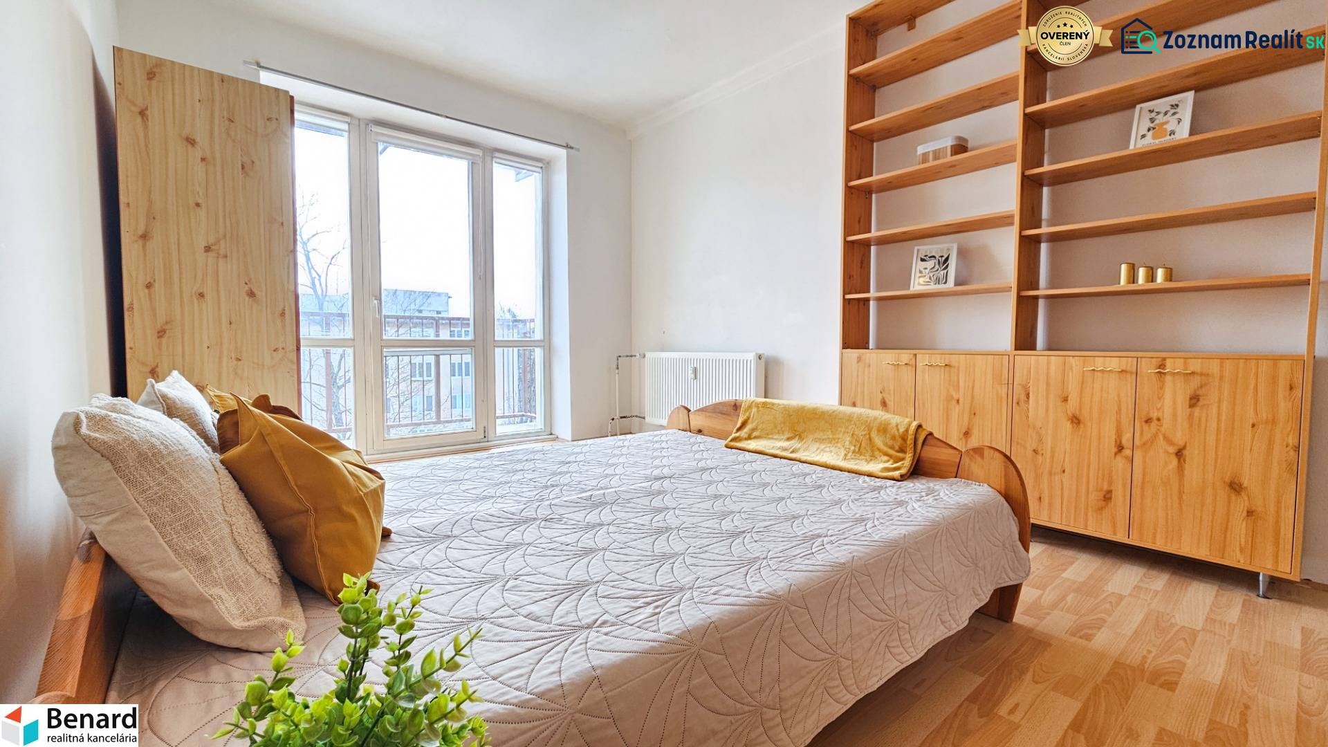 Světlá ložnice v 2-pokojovém bytě s postelí, policovou skříní a podlahou s dřevěným dekorem.