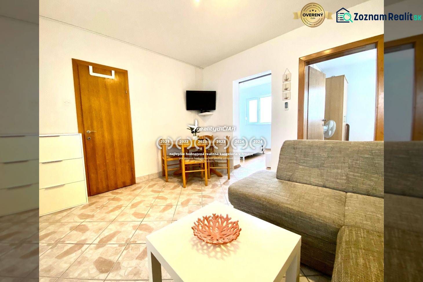 Obývací pokoj v rodinném domě s pohovkou, stolkem a televizí na stěně.