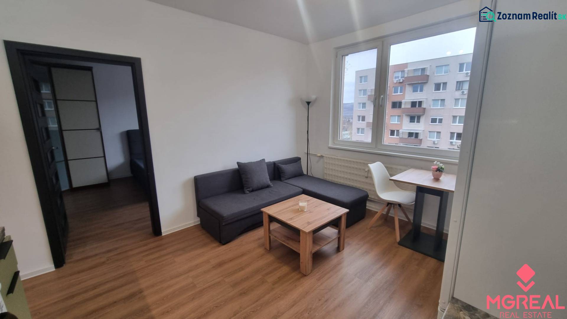 Obývací pokoj v jednopokojovém bytě s pohovkou, stolem, židlí a podlahou s dřevěným dekorem.