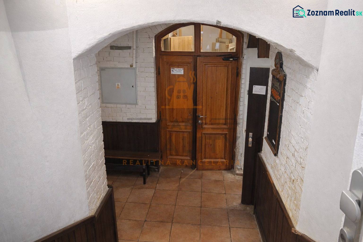 Vstupní dveře v obchodních prostorách s cihlovou stěnou a dlažbovou podlahou.