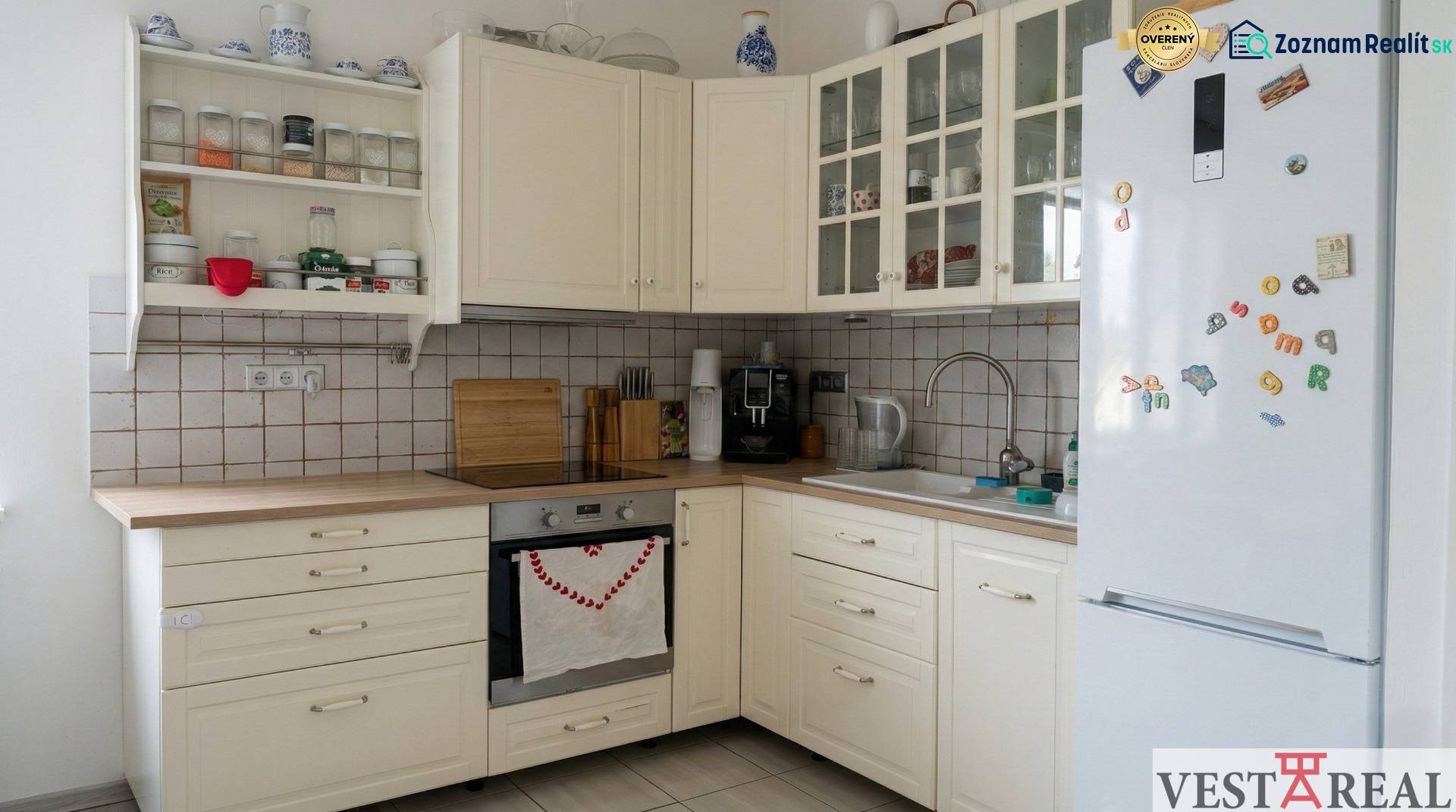 Kuchyně v 2-pokojovém bytě s bílými skříňkami a spotřebiči, podlaha s dřevěným dekorem.