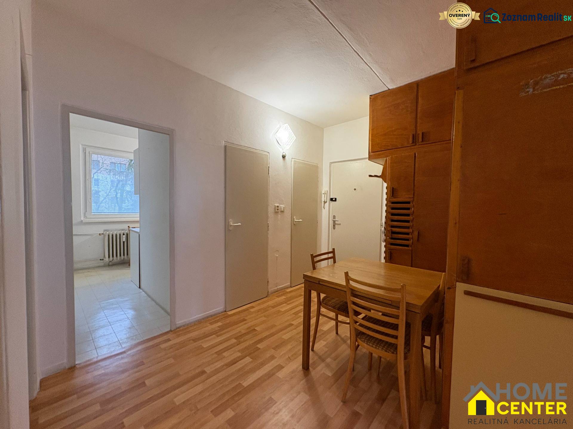 Interiér 3-pokojového bytu s podlahou s dřevěným dekorem, jídelní kout se stolem a židlemi.