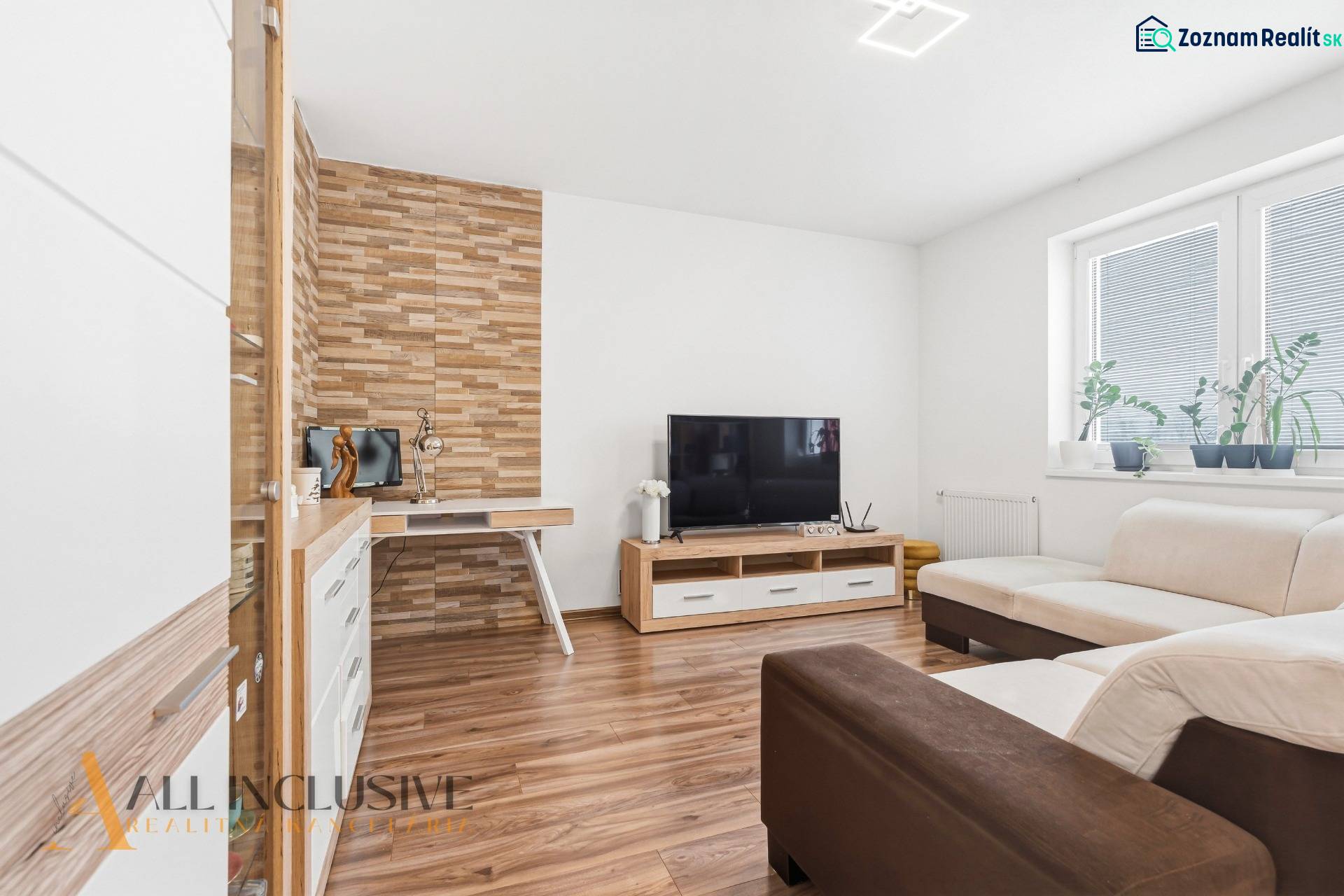 Obývací pokoj s podlahou s dřevěným dekorem, TV a krémovou sedačkou v 2pokojovém bytě.