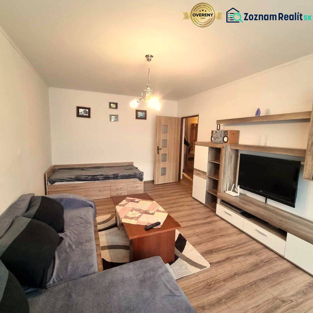 Obývací pokoj s podlahou s dřevěným dekorem v 2-pokojovém bytě, pohovka a televizor.