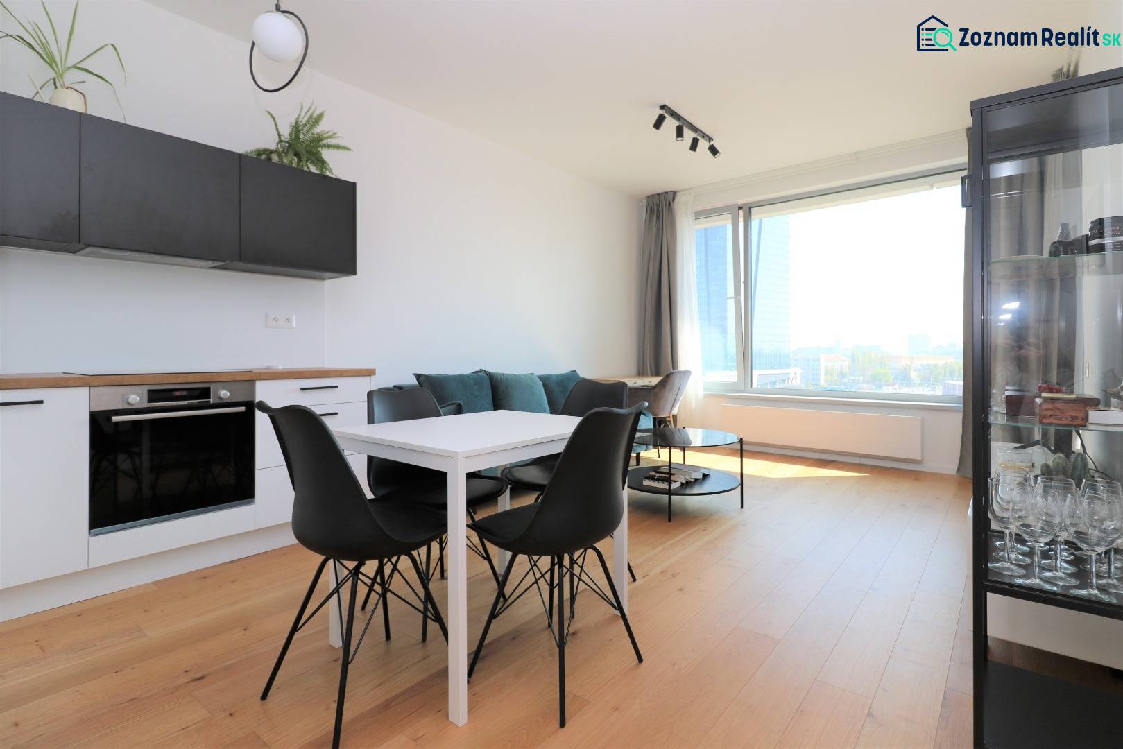 Kuchyně a jídelní stůl s černými židlemi v dvoupokojovém bytě s podlahou s dřevěným dekorem.