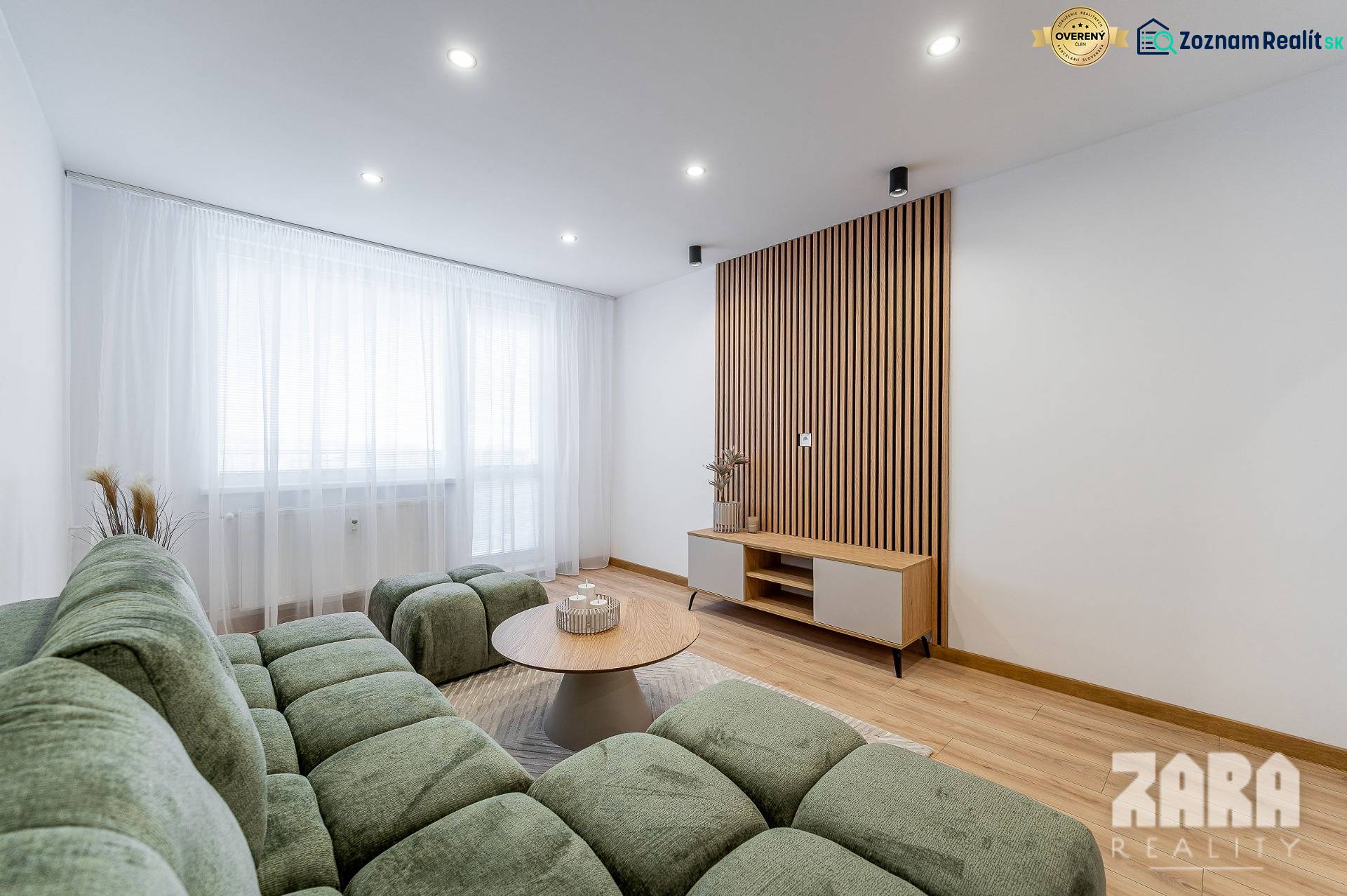 Obývací pokoj s podlahou s dřevěným dekorem, zelenou sedačkou a světlým nábytkem v 2-pokojovém bytě.