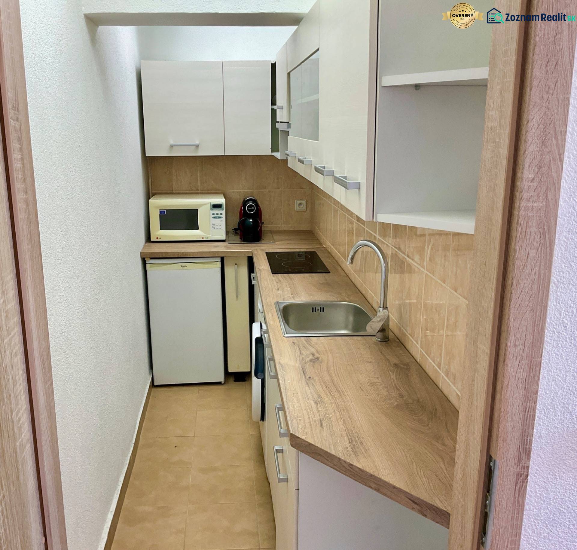 Kuchyně v 1-pokojovém bytě s dřevěným dekorem, mikrovlnkou a vestavěnými spotřebiči.