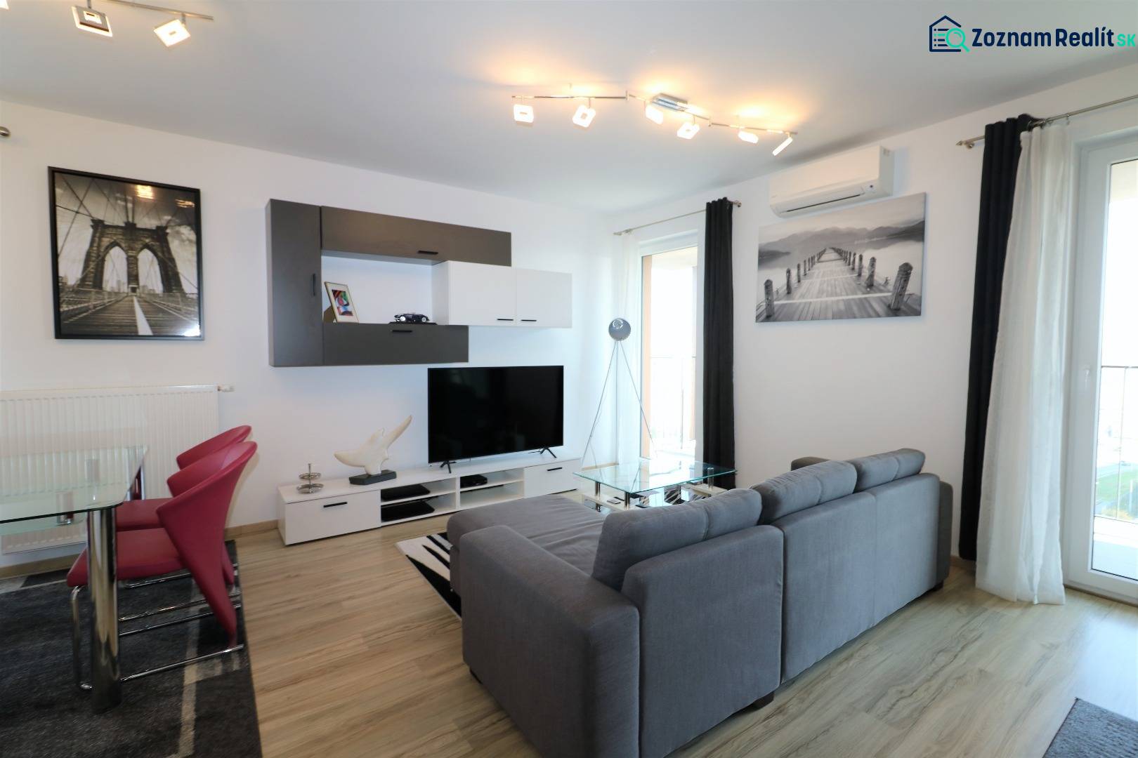 Obývací pokoj v 2-pokojovém bytě s pohovkou, TV, podlahou s dřevěným dekorem.