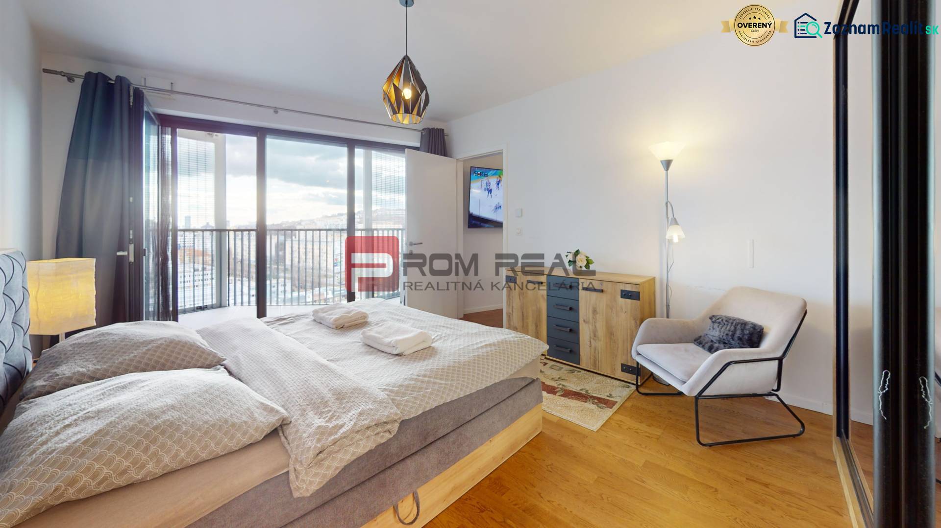 Ložnice s velkou postelí, křeslem a skříní, podlaha s dřevěným dekorem.