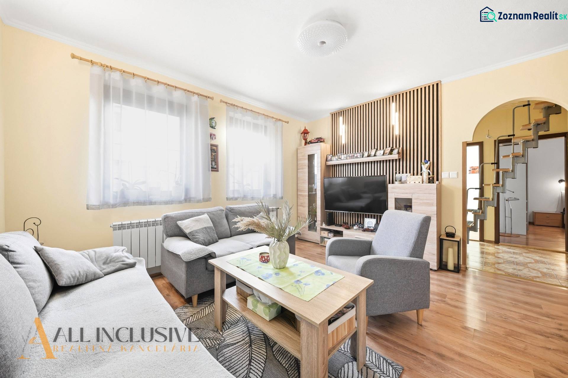 Obývací pokoj v rodinném domě s pohovkou, stolkem, televizí a podlahou s dřevěným dekorem.