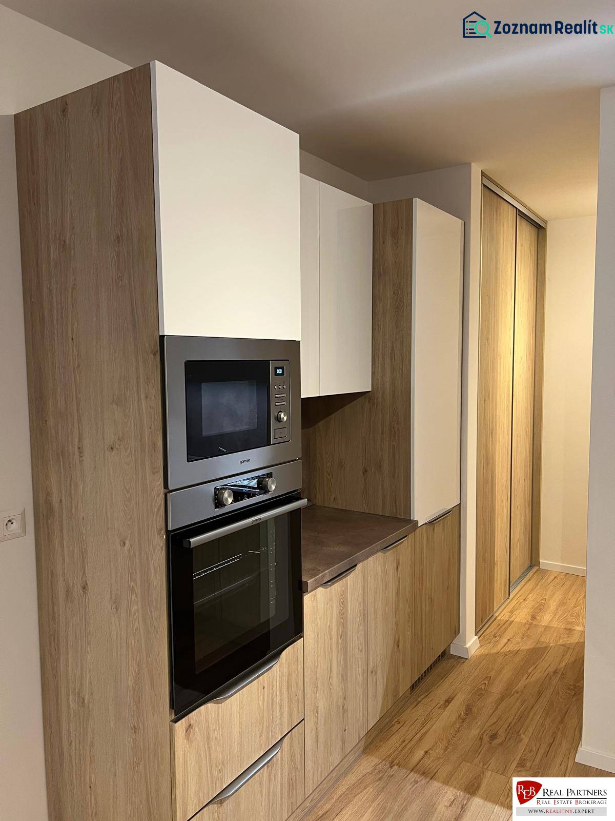 Kuchyňská část dvoupokojového bytu s podlahou s dřevěným dekorem a vestavěnými skříňkami.