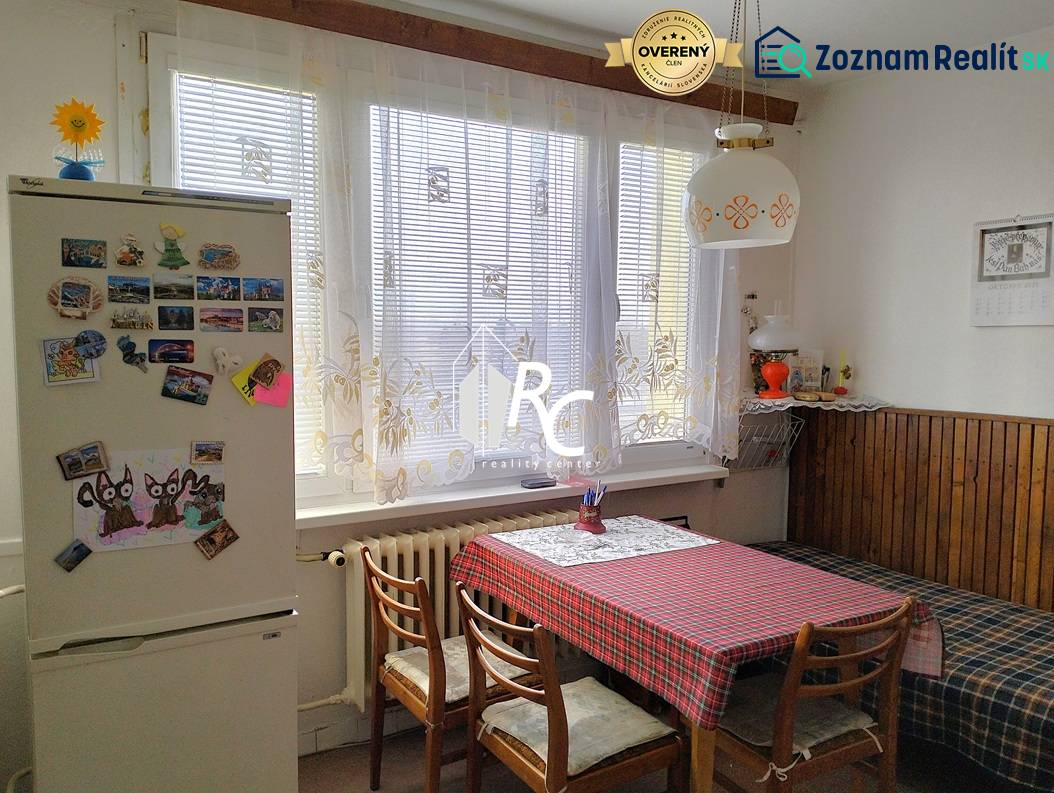 Kuchyně v 2-pokojovém bytě s jídelním stolem, židlemi a lednicí s magnetkami.