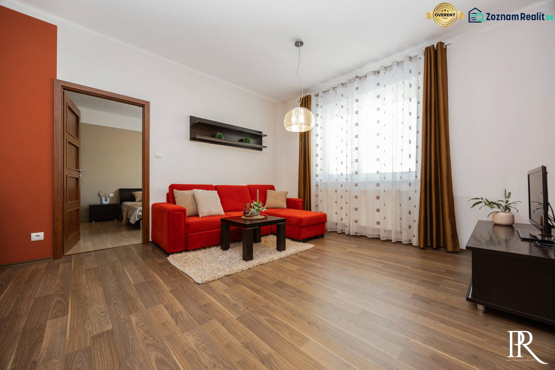Obývací pokoj v 2pokojovém bytě s červenou pohovkou a podlahou s dřevěným dekorem.